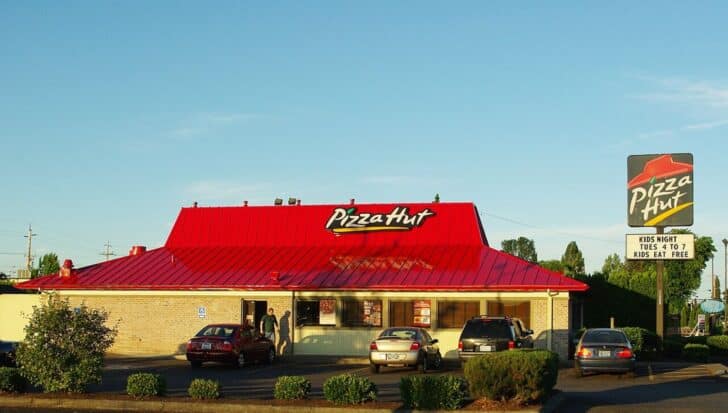 Exterior of a Pizza Hut restaurant with a red roof and several cars parked outside, displaying a sign advertising Kids Night